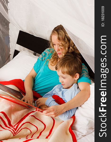Beautiful young woman reading book with her son on a bed. Beautiful young woman reading book with her son on a bed