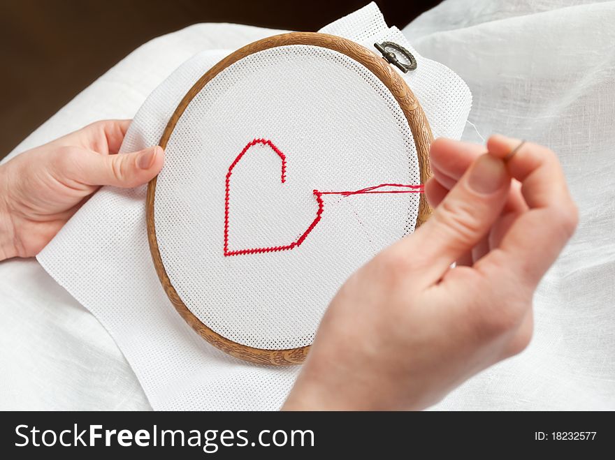 A female hands embroidering red heart. A female hands embroidering red heart