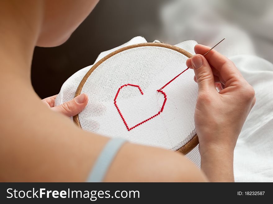 Young woman embroidering a red heart. Young woman embroidering a red heart