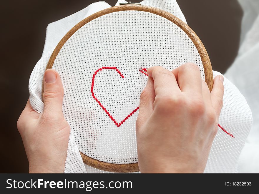 Female hands with tambour and needle, embroidering valentine heart