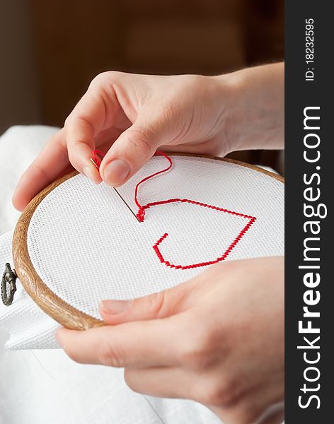 A female hands embroidering red heart. A female hands embroidering red heart