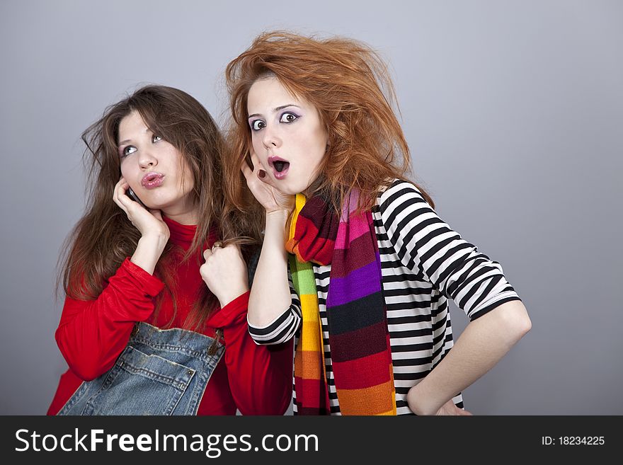 Two funny girls. One of them calling by phone. Studio shot.