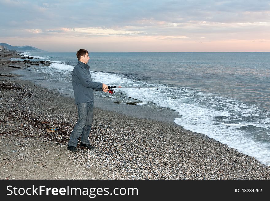 Fisherman on the shore of evening sea