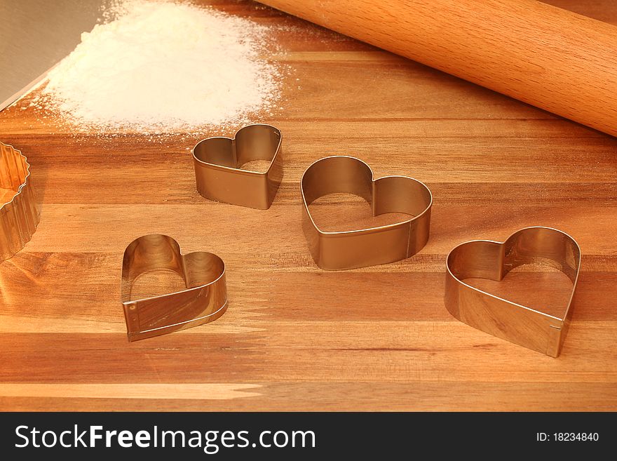 Heart shaped cookie cutters, rolling pin & sifted flour on cutting board