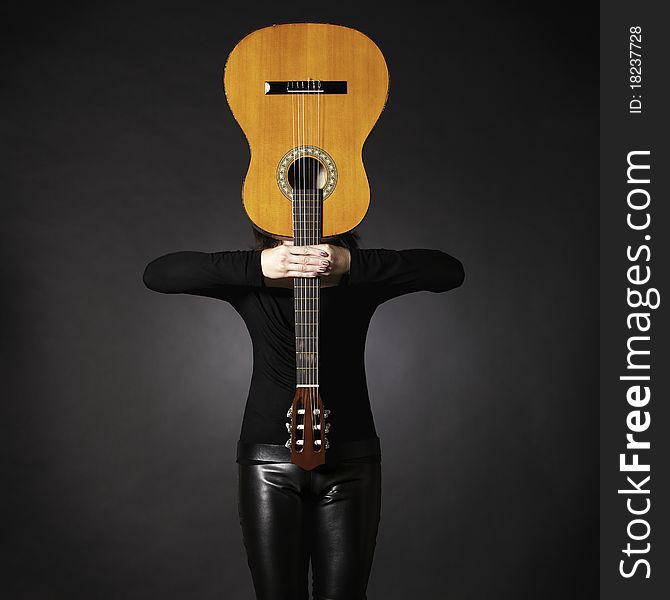 Woman in black holding guitar in front of face, creating a cross shape, isolated on black background. Woman in black holding guitar in front of face, creating a cross shape, isolated on black background.