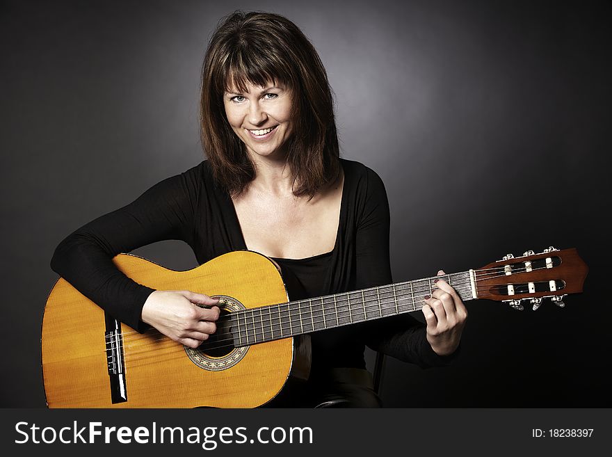 Smiling girl in black sitting and playing on guitar looking straight, isolated on black background. Smiling girl in black sitting and playing on guitar looking straight, isolated on black background.