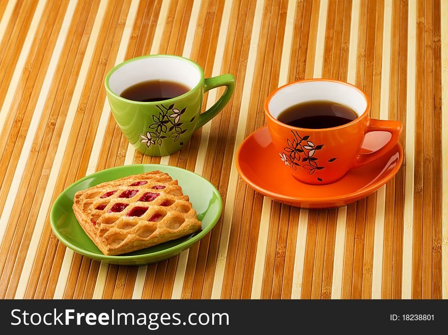 Tea in a bright cups and puff bun with jam in a saucer. Tea in a bright cups and puff bun with jam in a saucer.