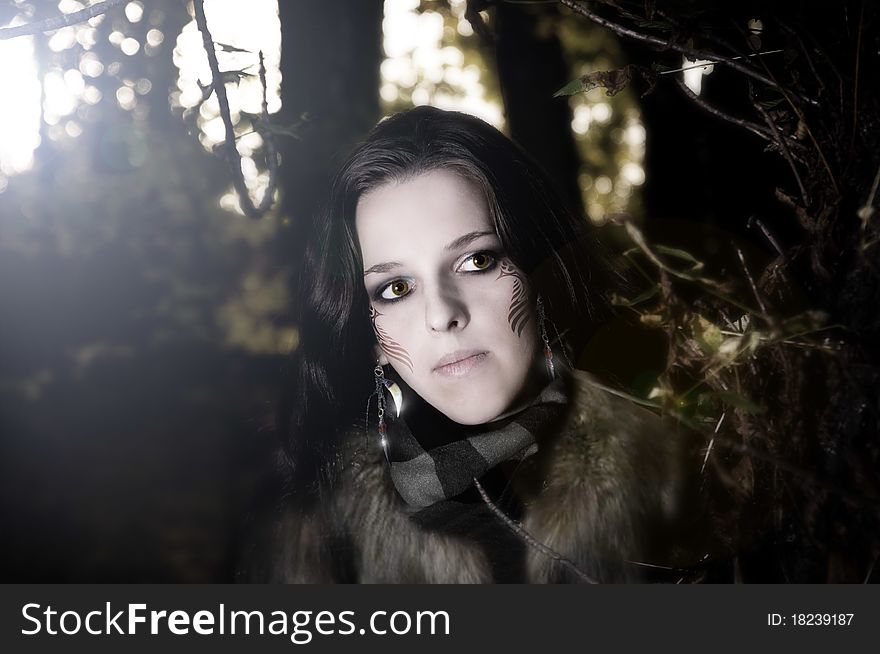 Mysterious young woman with wild clothes, make-up and paint on her face in dark forest. Mysterious young woman with wild clothes, make-up and paint on her face in dark forest.