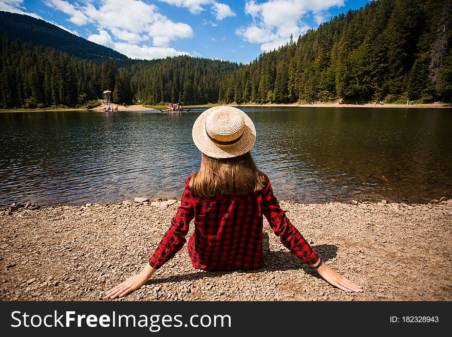 Tourist woman in hat sitting backwards and watching magic lake in mountainous country landscape