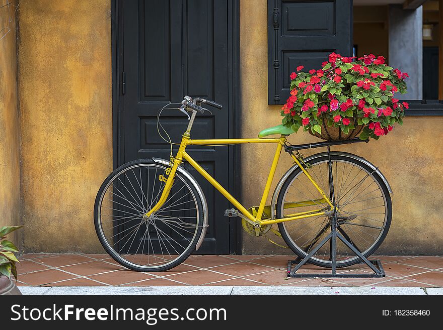 Yellow vintage bike with basket full of red flowers next to an old building in Danang, Vietnam, close up