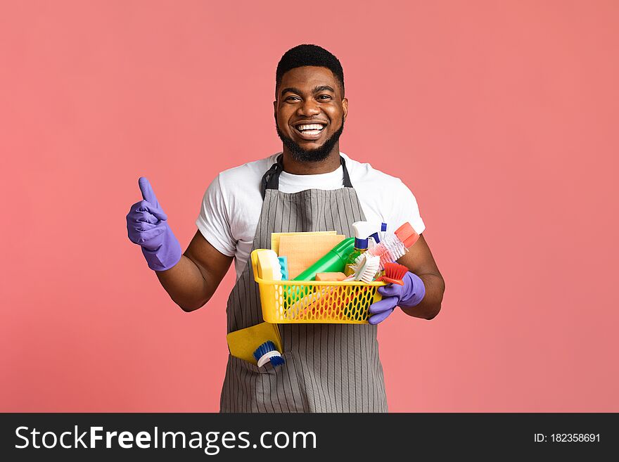 Cleaning With Pleasure. Positive Black Man Holding Container With Detergents And Household Supplies And Showing Thumb Up Over Pink Background. Cleaning With Pleasure. Positive Black Man Holding Container With Detergents And Household Supplies And Showing Thumb Up Over Pink Background