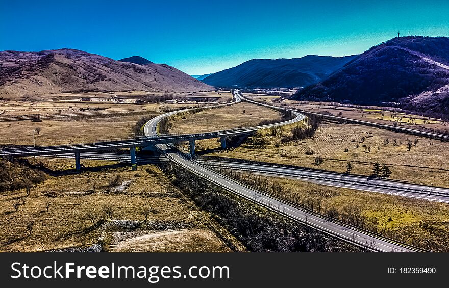 Aerial view of a highway intersection in a rural and mountainous area. We are in the daytime and the road is not very busy. Aerial view of a highway intersection in a rural and mountainous area. We are in the daytime and the road is not very busy