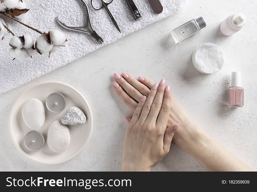 Woman`s hands with delicate pink manicure on the background of manicure tools. nails salon and spa. White concrete background, top view