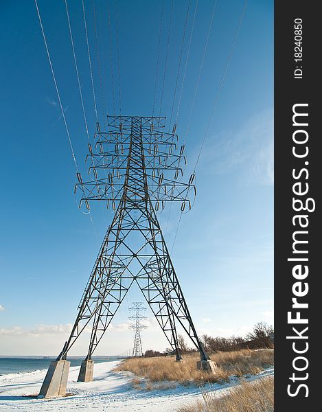 An electrical transmission tower carrying high voltage lines beside a lake in winter. An electrical transmission tower carrying high voltage lines beside a lake in winter.