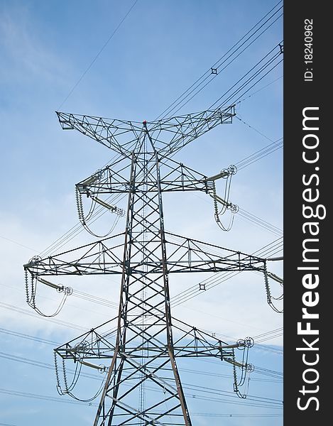 A transmission tower carrying high-voltage electrical lines stands against a blue sky. A transmission tower carrying high-voltage electrical lines stands against a blue sky.