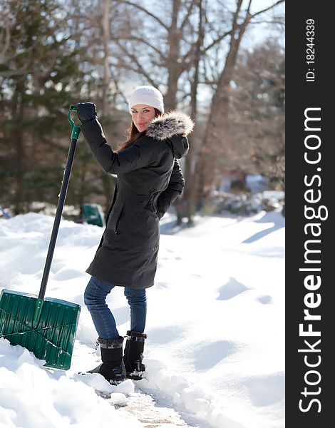 An attractive young woman looks over her shoulder and smiles while taking a break from shoveling snow. An attractive young woman looks over her shoulder and smiles while taking a break from shoveling snow