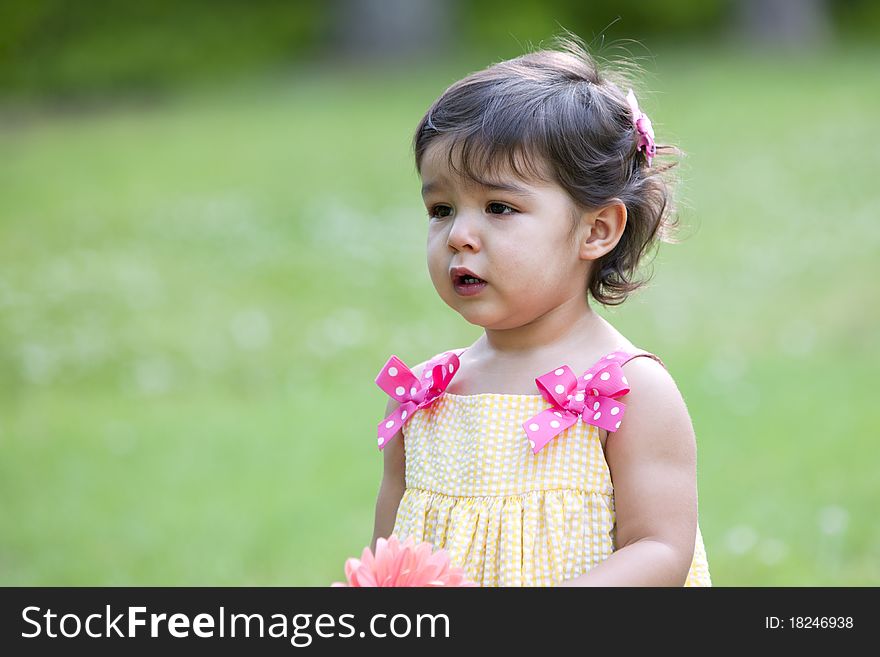 Beautiful little brunette girl outdoors with a questioning expression on her face and wearing a yellow sundress with pink dotted bows. Beautiful little brunette girl outdoors with a questioning expression on her face and wearing a yellow sundress with pink dotted bows