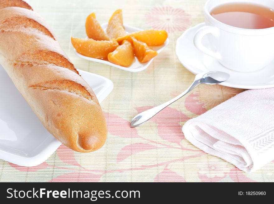 Crisp fresh-baked baguette on white plate, peach dessert and a cup of tea on bamboo placemat. Crisp fresh-baked baguette on white plate, peach dessert and a cup of tea on bamboo placemat