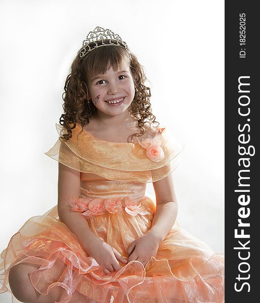 The girl the princess in a orange dress sits opposite to a white background. The girl the princess in a orange dress sits opposite to a white background