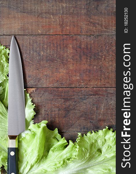 Kitchen knife and green leaves of lettuce lying on wooden surface with copy space. Kitchen knife and green leaves of lettuce lying on wooden surface with copy space