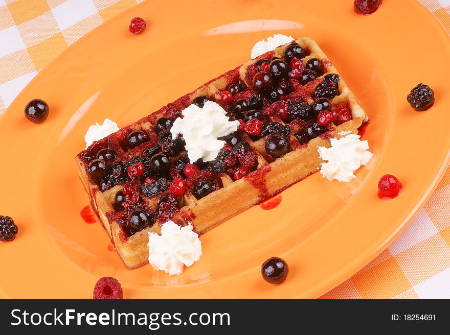 Waffle with soft fruits and whipped cream served on an orange plate. Studio shot, selective focus