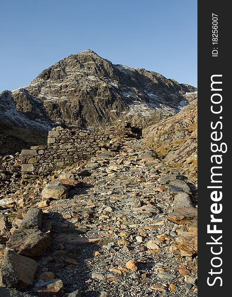 A rocky footpath leads up towards a mountain peak with large cliffs and ridgelines. A rocky footpath leads up towards a mountain peak with large cliffs and ridgelines.