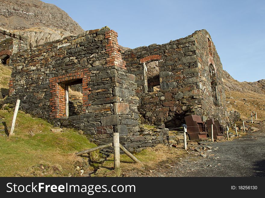 The derelict ruins of an historical copper mine with a protective fence and mountain in the high distance. The derelict ruins of an historical copper mine with a protective fence and mountain in the high distance.