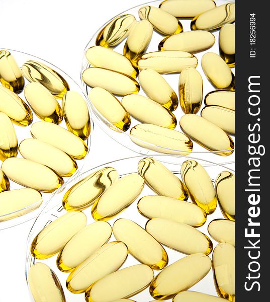 Gold pills or capsules backlit on white for medical or science use in petri dishes. Gold pills or capsules backlit on white for medical or science use in petri dishes