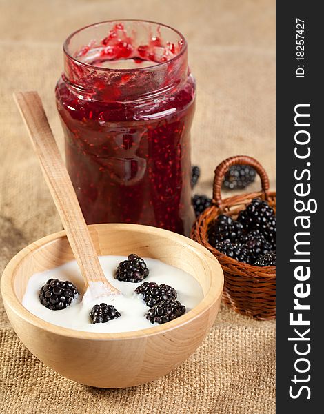 Wooden bowl of Yogurt and blackberries with pot of jam on sackcloth. Wooden bowl of Yogurt and blackberries with pot of jam on sackcloth