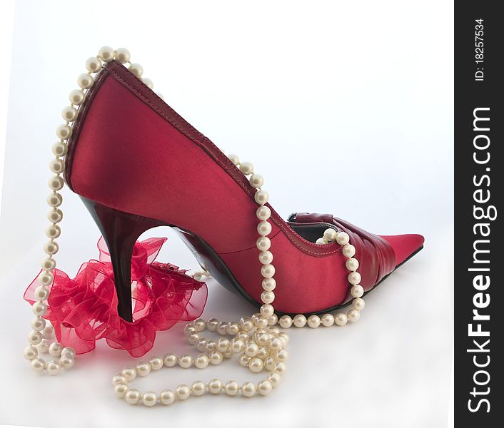 One red shoe with red garter for stocking and pearls on white background