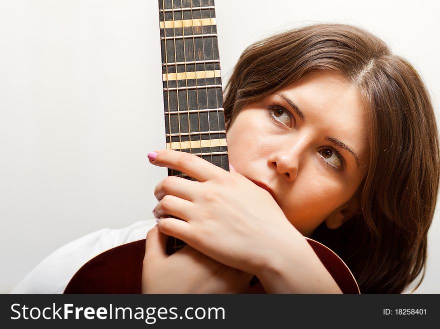 Young woman in white clothes holding guitar's neck in her arms. Young woman in white clothes holding guitar's neck in her arms