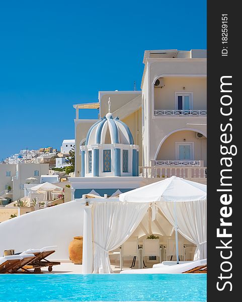 Colorful street with traditional architecture on island of Santorini in Oia, Greece. In front is swimming pool with a sunshade and in a background small belfry. Colorful street with traditional architecture on island of Santorini in Oia, Greece. In front is swimming pool with a sunshade and in a background small belfry.