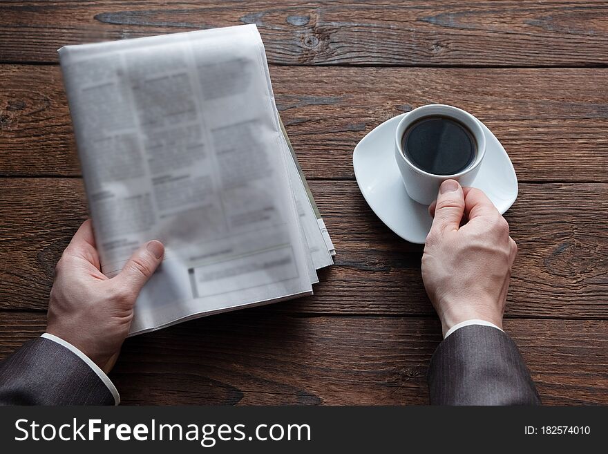 Top view on male hands holding a German newspaper and a cup of black coffee. Reading the news in the morning.  Finance, business. Place for text.