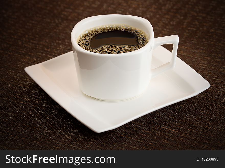 Dark coffee cup with brew on the top. White vessel with saucer dishware. Shallow depth of field and added vignetting. Dark coffee cup with brew on the top. White vessel with saucer dishware. Shallow depth of field and added vignetting.