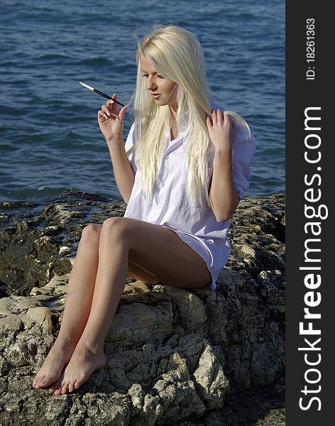 Speaking blonde in white with a cigarette near blue sea. Speaking blonde in white with a cigarette near blue sea