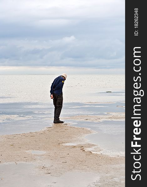 Man walking in tidal flat under clouds