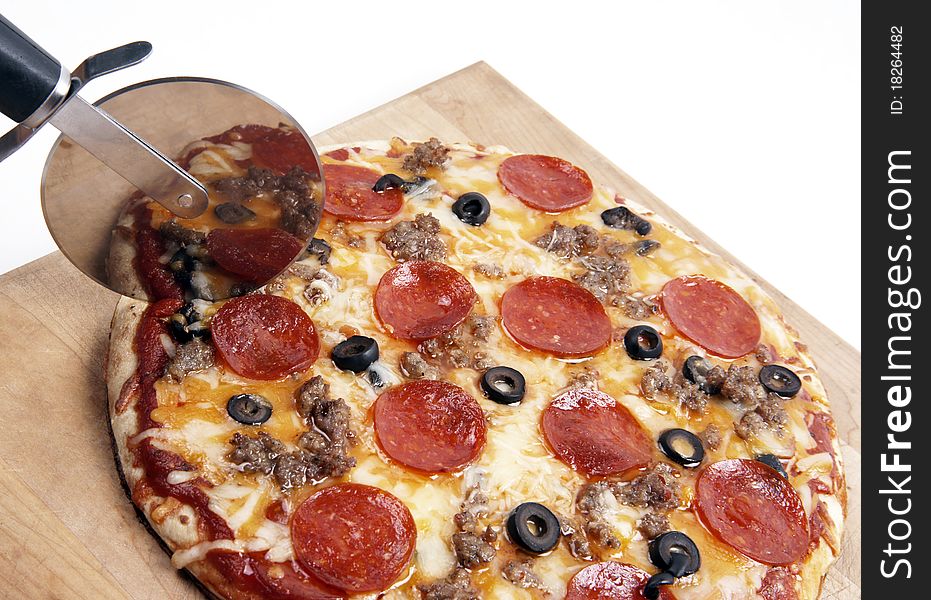 A freshly baked pizza sitting on the cutting board being cut into pieces. A freshly baked pizza sitting on the cutting board being cut into pieces