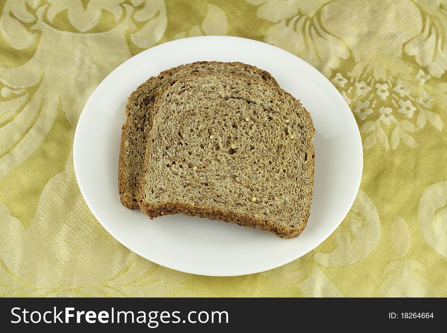 Two crisp whole sprouted grain and legume bread slices on a round white dish above a buttery yellow floral cloth placemat. Two crisp whole sprouted grain and legume bread slices on a round white dish above a buttery yellow floral cloth placemat.