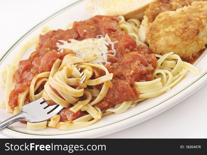 A plate full of fettucini with homemade marinara sauce and parmesan crusted chicken, selective focus on fork, delicious. A plate full of fettucini with homemade marinara sauce and parmesan crusted chicken, selective focus on fork, delicious