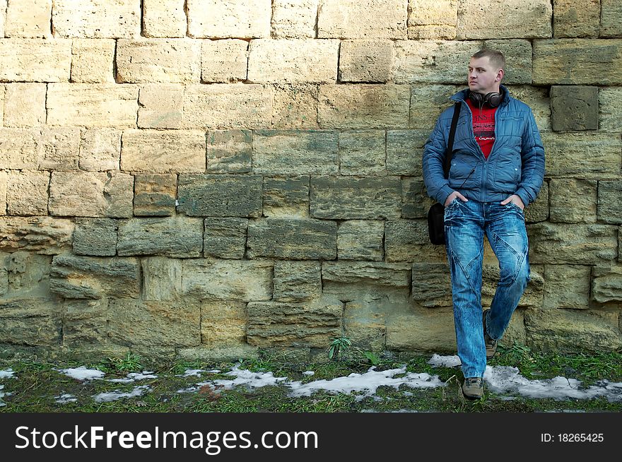 The guy with earphones stand near a brick wall. The guy with earphones stand near a brick wall