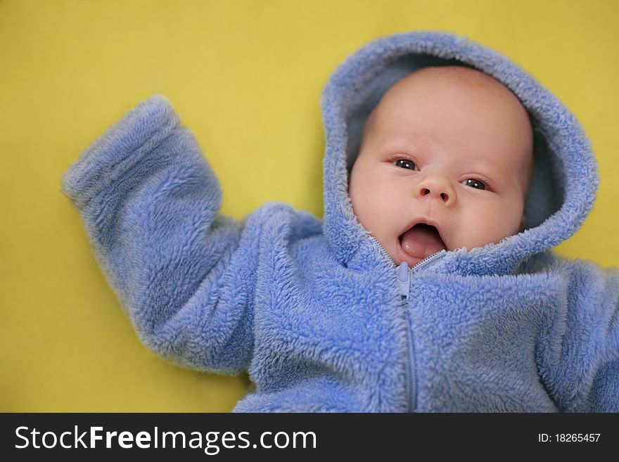 The cheerful baby in blue overalls on a yellow background (Small depth of sharpness). The cheerful baby in blue overalls on a yellow background (Small depth of sharpness)