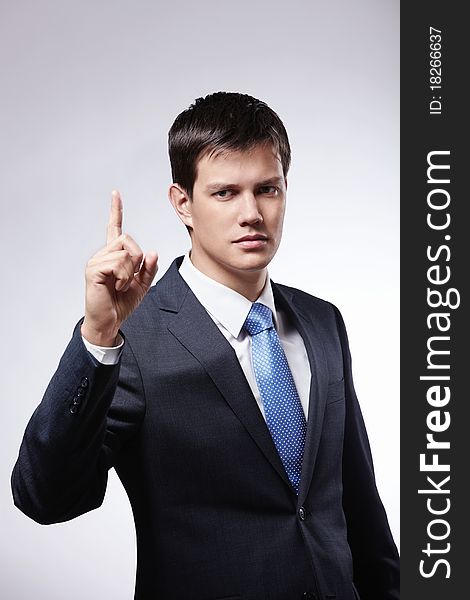 Attractive man in a suit with the index finger up on a gray background. Attractive man in a suit with the index finger up on a gray background