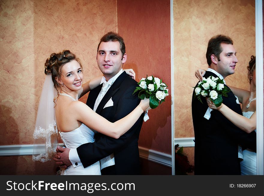 Happy bride and groom near mirror in wedding day in luxury palace