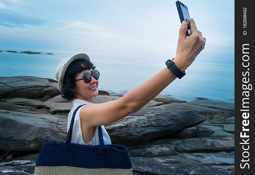 Female travelers take a picture with a smartphone in a seaside tourist spot in Thailand.