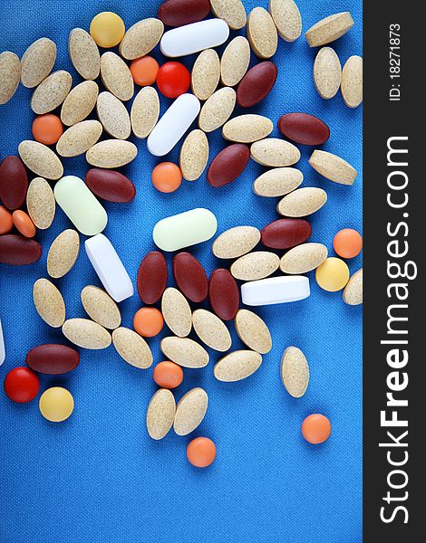 A group of various pills sit on a blue background. A group of various pills sit on a blue background.