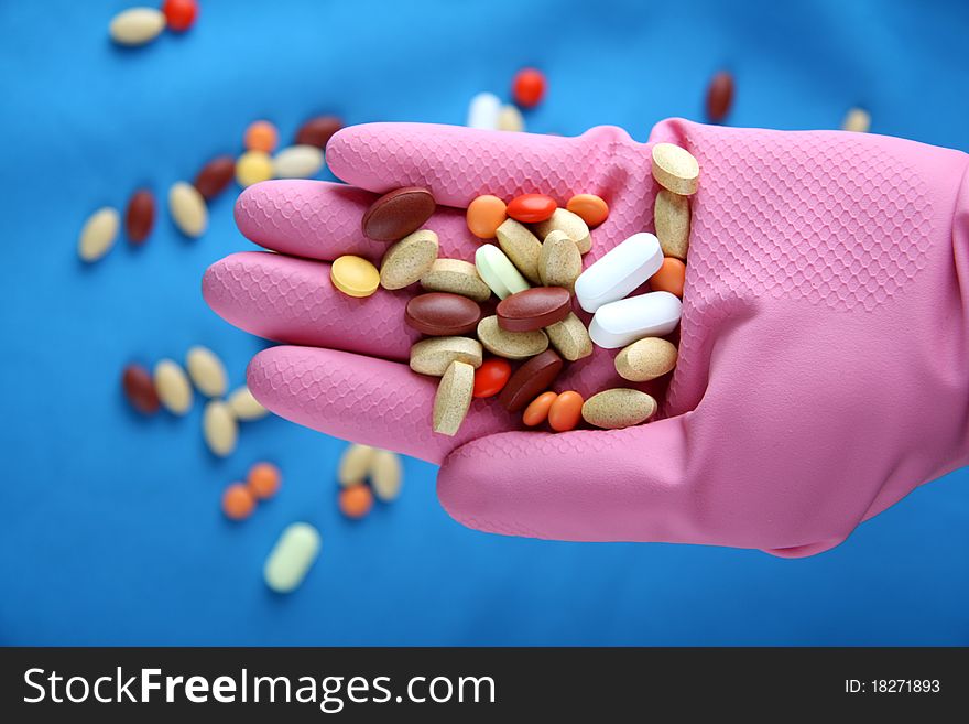 A group of various pills sit pink gloves and blue background. A group of various pills sit pink gloves and blue background.