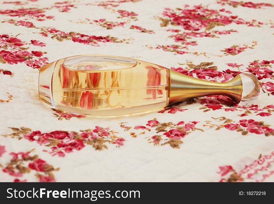 Bottle of perfume on white cloth with pattern of flowers. Bottle of perfume on white cloth with pattern of flowers