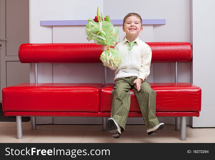 Little funny boy with flowers sitting on the couch