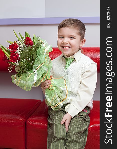 Little funny boy with flowers sitting on the couch