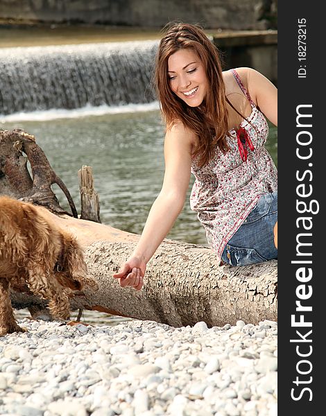 Young brunette woman sitting outside at a river playing with her dog. Young brunette woman sitting outside at a river playing with her dog